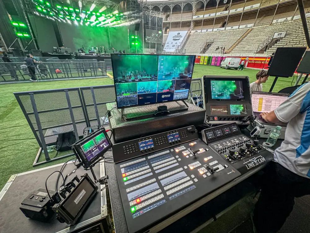 Puesto de realización con panel de mezcla ATEM y multiviewer frente al escenario de un concierto en una plaza de toros