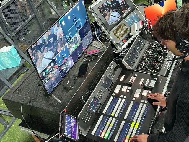Realizador operando el panel de mezcla ATEM durante un festival, con el multiviewer y el público al fondo